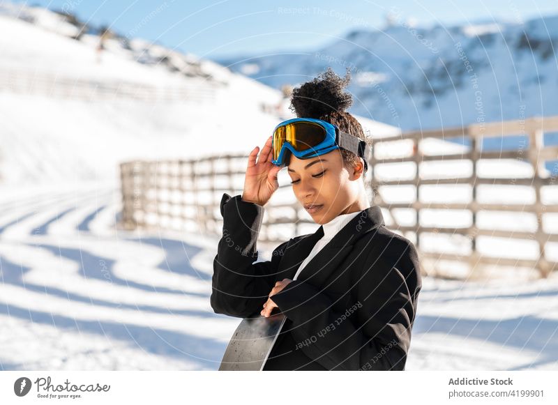 Stylish black sportswoman with snowball on snowboard winter stylish glasses friendly enjoy show suit trendy boot wintertime cold weather equipment athlete