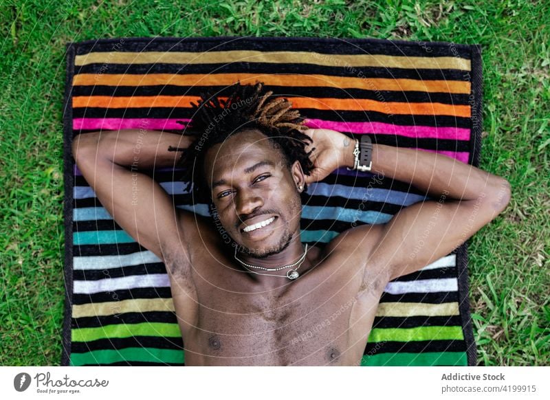 Smiling black man relaxing on towel on grass lying summer vacation enjoy smile carefree male ethnic african american naked torso shirtless meadow happy positive