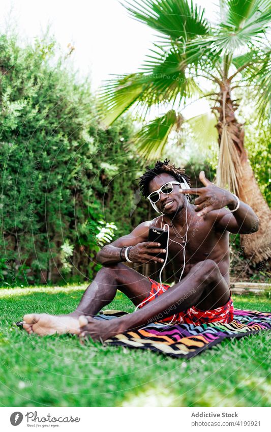 Cool black man showing rock gesture listen music taking headphones selfie rock and roll horn smile cool male ethnic african american summer park towel gadget