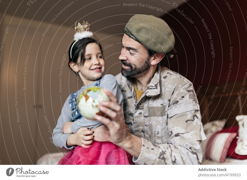 Smiling father pointing at place on globe daughter soldier explain army defense serve military girl man dad speak defend map kid uniform security power national