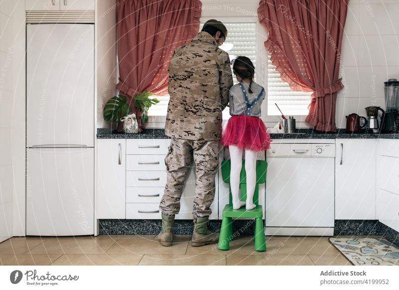 Military man standing at counter with daughter in kitchen military father together soldier home serviceman wash homecoming arrive love child male kid girl house