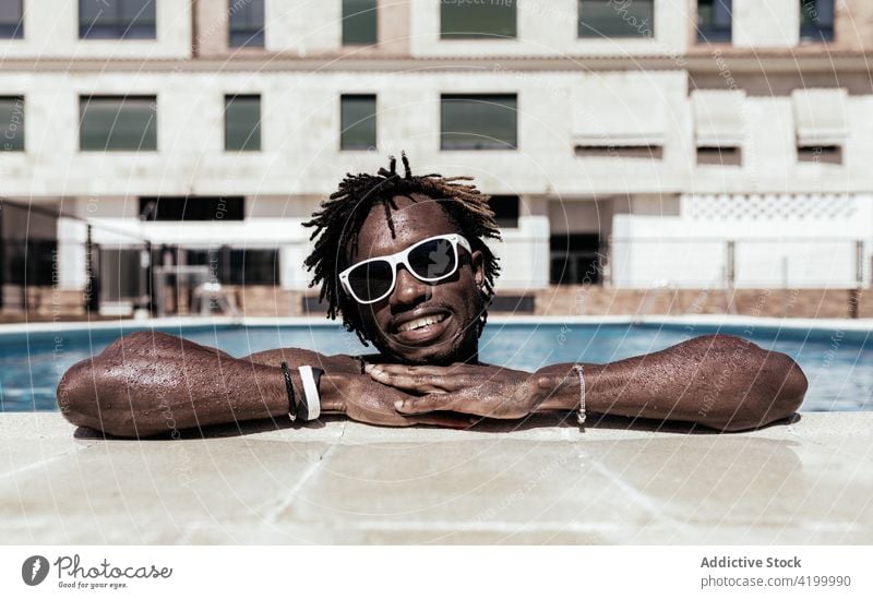 Cheerful black man in swimming pool in summer poolside cheerful sunglasses enjoy vacation sunny holiday male ethnic african american happy delight optimist