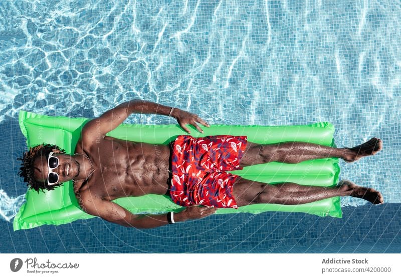Black man relaxing on inflatable mattress in pool carefree summer vacation enjoy smile male ethnic black african american shorts lying naked torso shirtless
