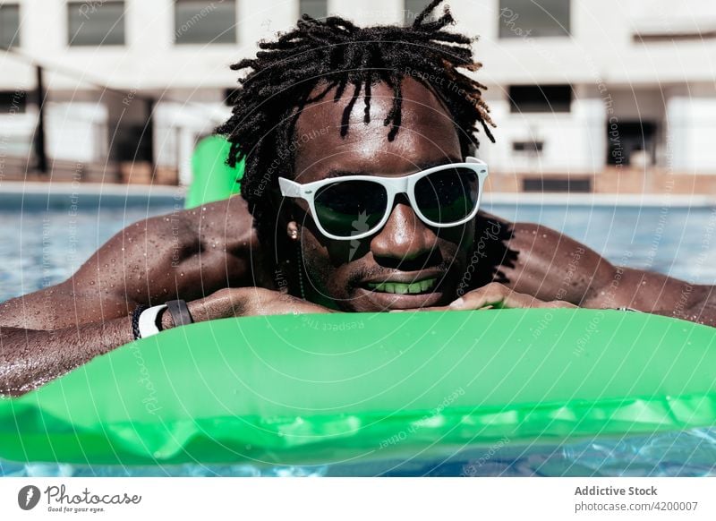 Black man in sunglasses in swimming pool inflatable mattress relax carefree summer vacation enjoy smile male ethnic black african american shorts lying