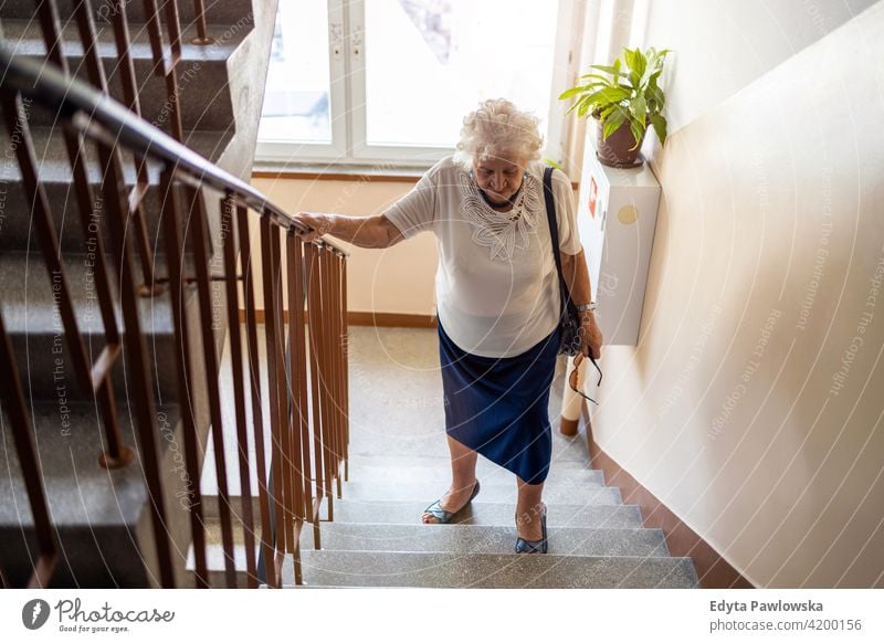 Senior woman climbing staircase with difficulty people senior mature casual female Caucasian elderly home house old aging domestic life grandmother pensioner