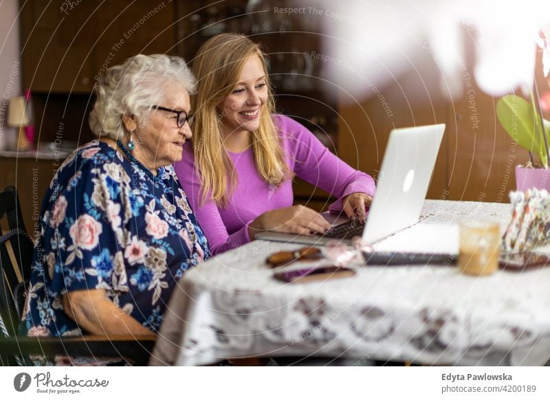 Adult granddaughter teaching her elderly grandmother to use laptop people woman senior mature casual female Caucasian home house old aging domestic life