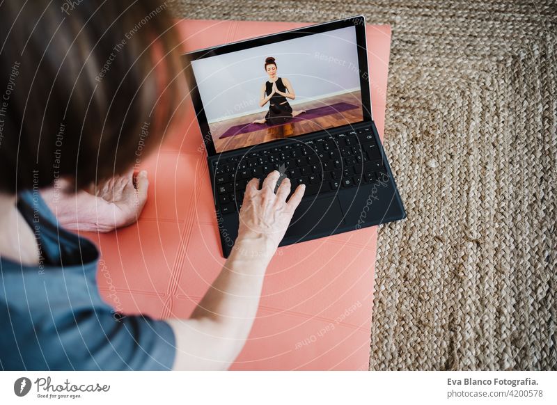 close up view of mature caucasian senior woman practicing yoga pose at home. using laptop for online class with teacher. Healthy and technology lifestyle sport