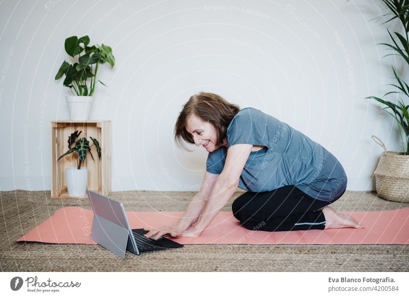 close up view of mature caucasian senior woman practicing yoga pose at home. using laptop for online class with teacher. Healthy and technology lifestyle sport