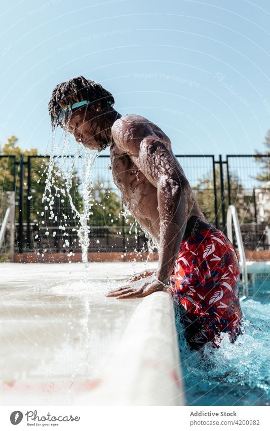 Black man splashing water in pool poolside lean emerge wet summer vacation male ethnic black african american swim activity resort aqua energy guy swimwear