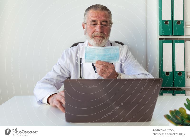 Senior doctor showing sterile mask against laptop during video call health care consultation online protect man using gadget prevent covid physician video chat