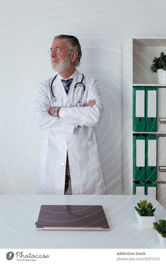 Elderly physician with crossed arms in hospital arms crossed self assured professional specialist uniform stethoscope man clinic portrait doctor robe tool