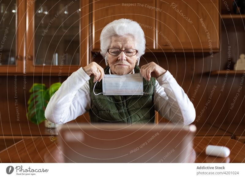 Elderly female showing sterile mask against laptop during video call woman health care consultation online protect using gadget prevent covid physician
