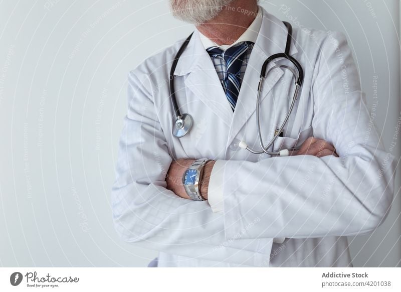 Elderly physician with crossed arms in hospital arms crossed self assured professional specialist uniform stethoscope man clinic portrait doctor robe tool