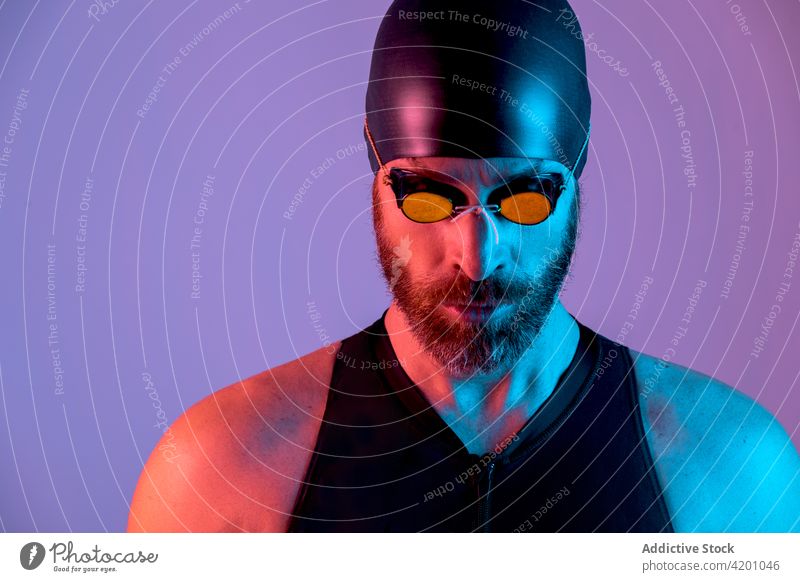 Portrait of a swimmer with cap and goggles looking down studio man portrait background glasses bearded healthy face young isolated white people one athlete
