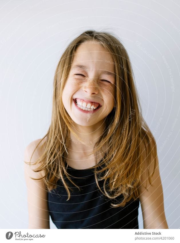 Happy girl with long hair and freckles against white background child laugh cheerful excited portrait fun joy humor delight positive toothy smile eyes closed