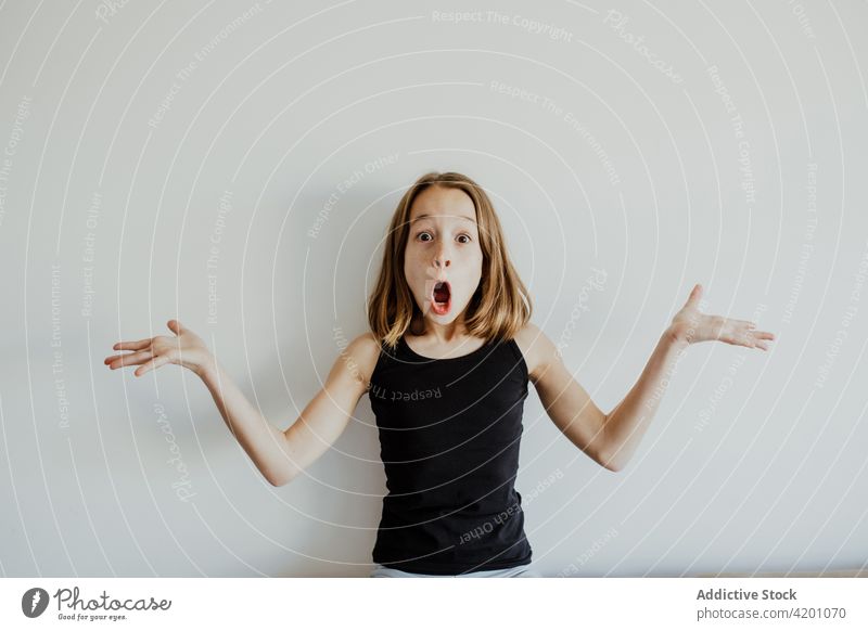 Excited girl making grimace against white wall child mouth opened amazed shock having fun shrug excited portrait joy funny kid casual positive happy expressive