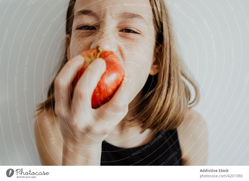 Delighted kid biting apple against white wall girl bite eat fresh fruit vitamin enjoy portrait meal ripe child preteen casual top human face daylight delicious