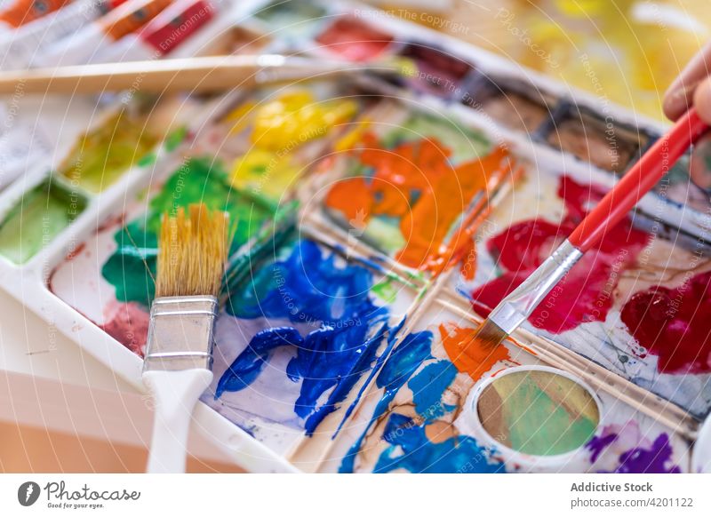 Crop artist blending aquarelle paints with brush in workroom painter mix palette paintbrush watercolor professional process painting collection colorful studio