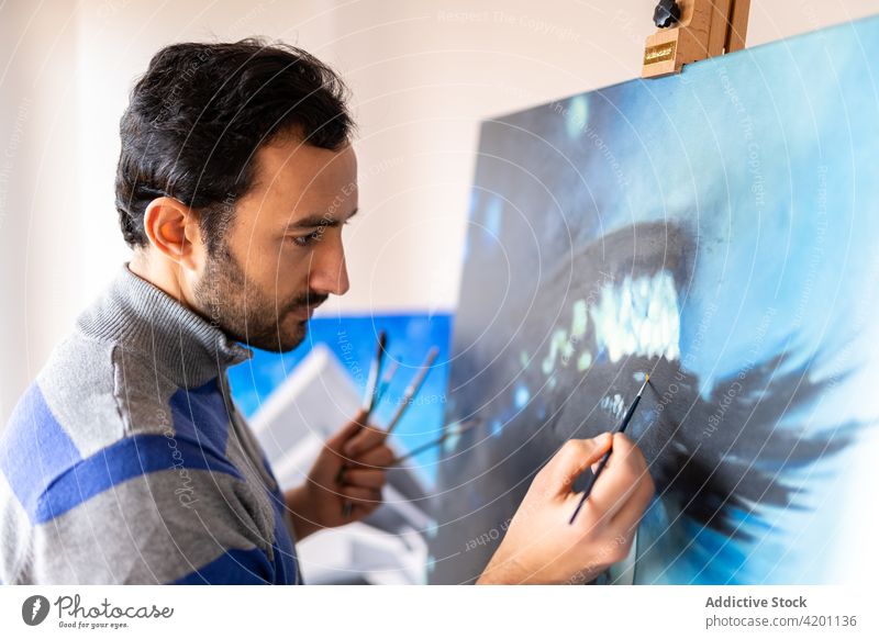 Hispanic male artist painting picture in workshop canvas artwork creative design talent professional man brush painter hispanic ethnic attentive casual wear