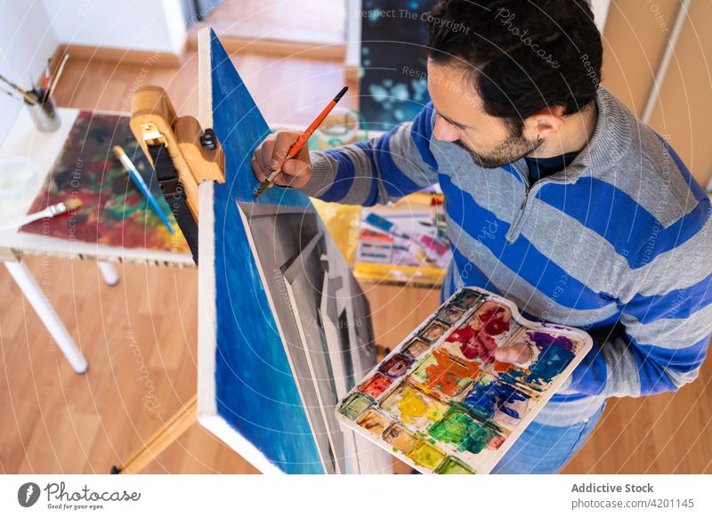 Hispanic male artist painting picture in workshop canvas artwork creative design talent professional man brush painter hispanic ethnic attentive casual wear