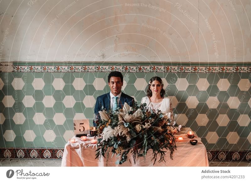 Multiethnic newlywed couple at table with decoration on wedding day marriage relationship festive celebrate restaurant portrait flower multiracial black number
