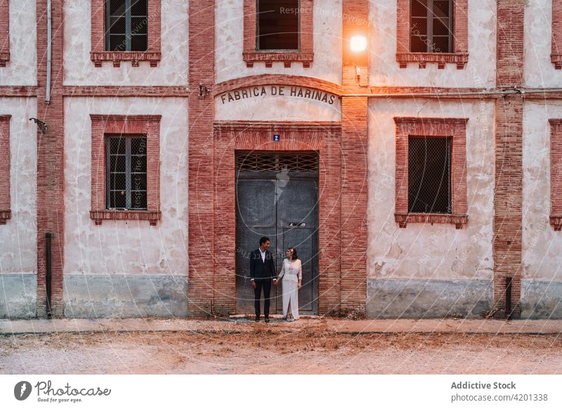 Romantic ethnic newlywed couple holding hands outside old brick building wedding tender brick wall amorous fancy marriage romantic calm contrast valentine