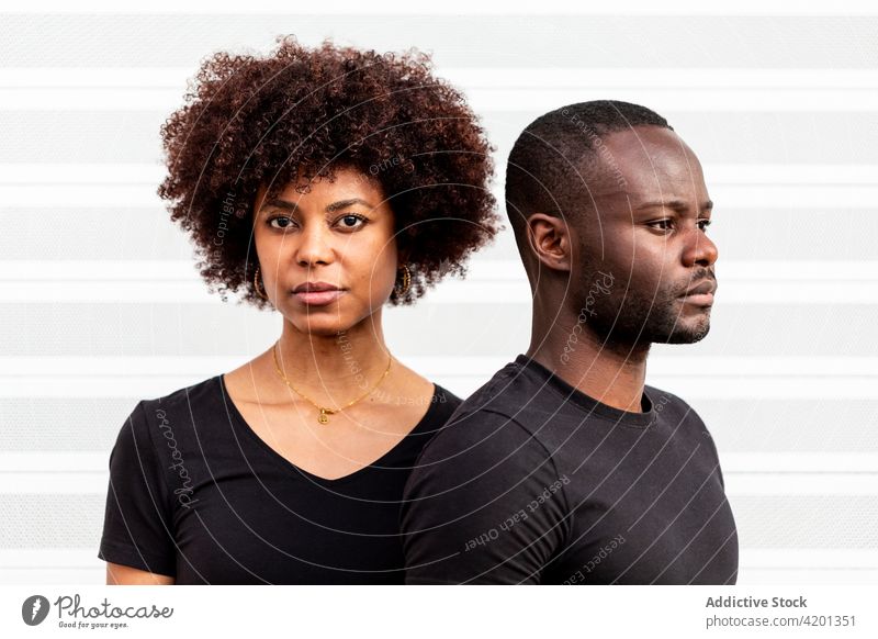 Serious black couple near striped wall in daytime serious sincere relationship casual style wistful afro portrait ornament hairstyle accessory pendant