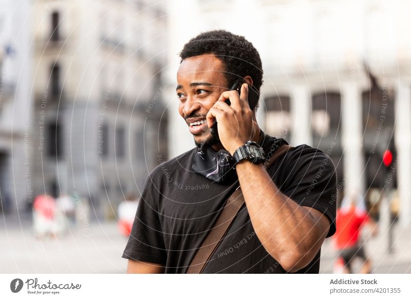 Smiling black man speaking on smartphone on city street smile friendly masculine conversation town portrait using gadget device wristwatch accessory casual
