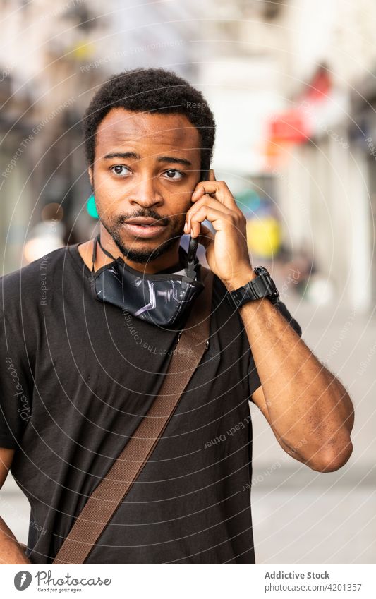 Smiling black man speaking on smartphone on city street friendly masculine conversation town portrait using gadget device wristwatch accessory casual cloth