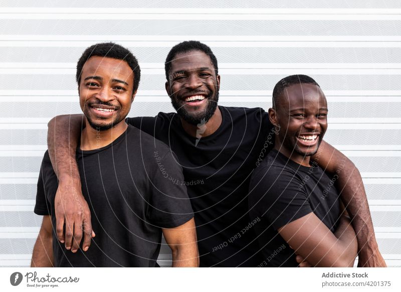 Cheerful black male friends embracing near striped wall best friend embrace cheerful sincere friendship happy blm movement portrait ornament justice equality