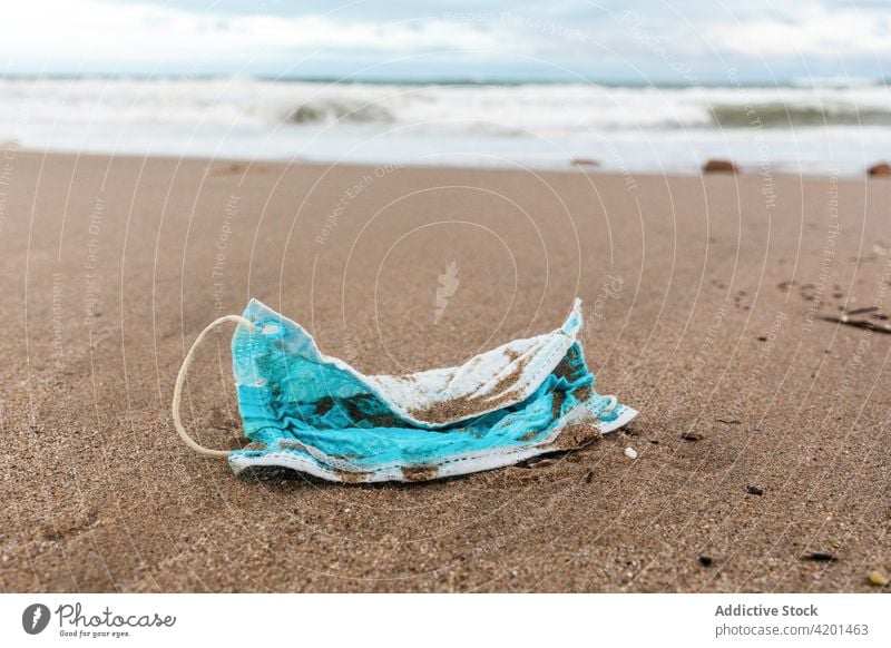 Dirty medical mask on sandy seashore pollute beach waste environment concept plastic trash garbage water rubbish used dirty protect wave shoreline seaside