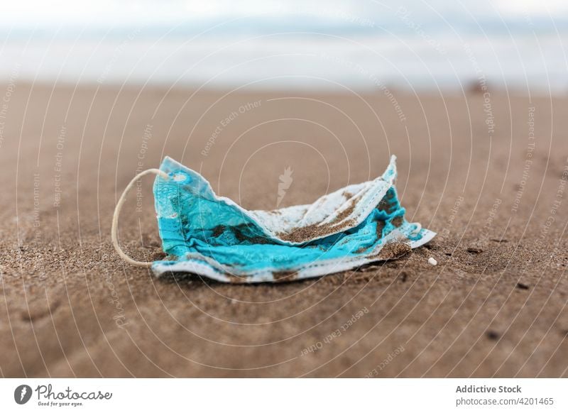 Dirty medical mask on sandy seashore pollute beach waste environment concept plastic trash garbage water rubbish used dirty protect wave shoreline seaside