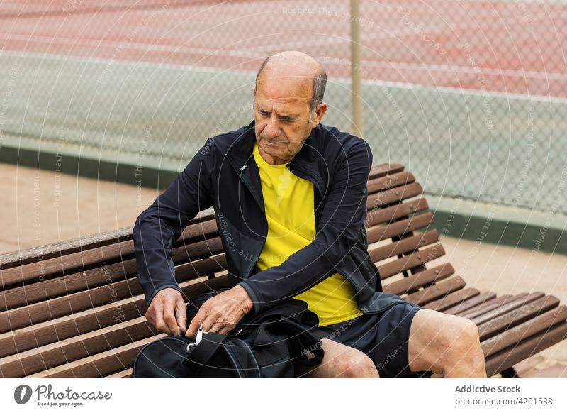 Senior man preparing for tennis workout sportsman bag open court prepare bench training sit male senior aged elderly sportswear activity break professional