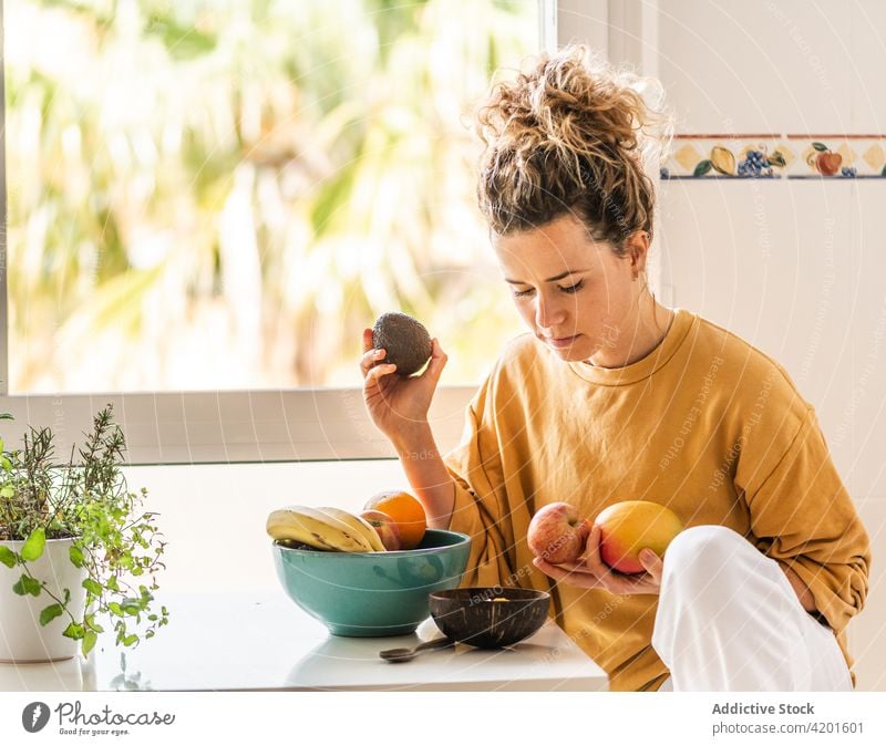 Pensive female choosing fruits for breakfast woman pensive thoughtful food choose fresh healthy wellness calm prepare room apartment at home table daylight
