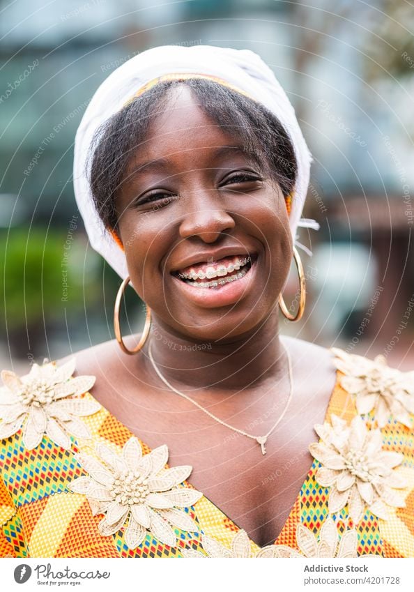 Happy black woman in ornamental apparel on city street style feminine smile elegant cheerful charming pleasant gentle happy portrait african ethnic floral wear