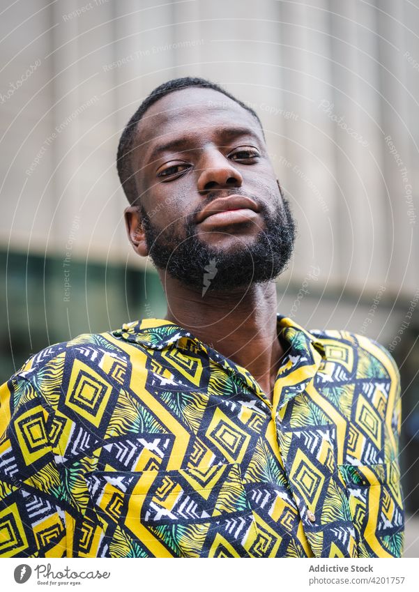 Black man standing on the street looking at camera friendly masculine macho ornament portrait city black african american ethnic shirt apparel unshaven enjoy