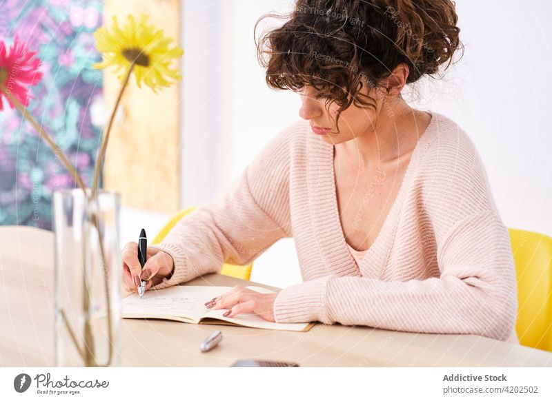 Thoughtful woman writing notes in copybook at home write notepad room take note smartphone vase flower thoughtful young female table casual notebook pen