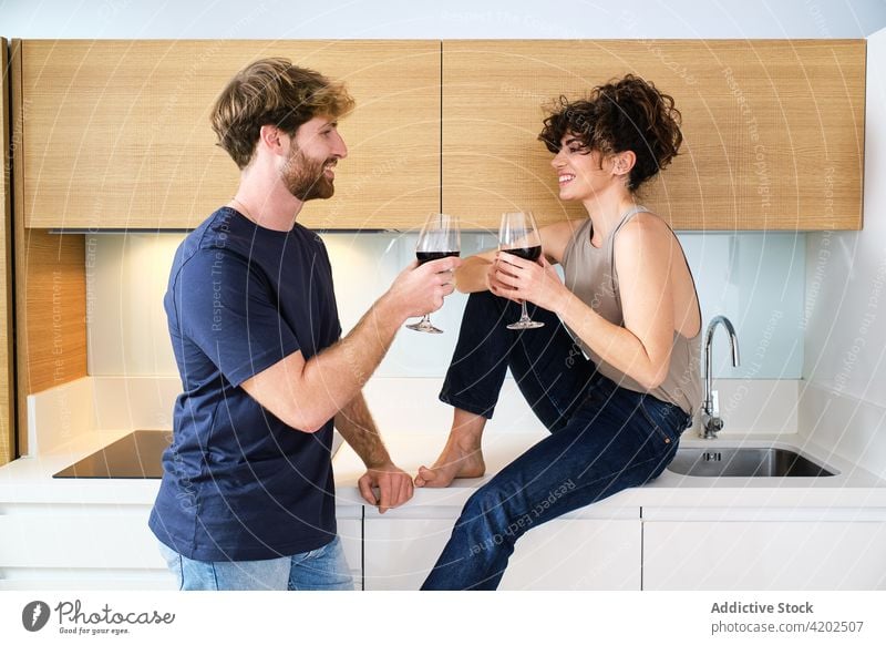 Couple drinking wine in kitchen from glasses couple relationship smile cheers girlfriend boyfriend young apartment red casual bright sink tap together home