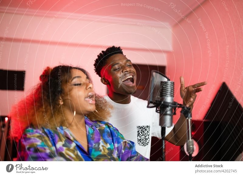 Black friends singing into microphone in studio vocalist eyes closed professional song music mouth opened duo singer musician enjoy equipment modern haircut
