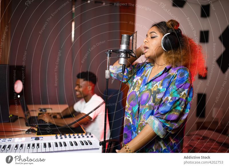 Black artist singing into microphone against producer with laptop singer record song music eyes closed using gadget device headphones netbook smile partner