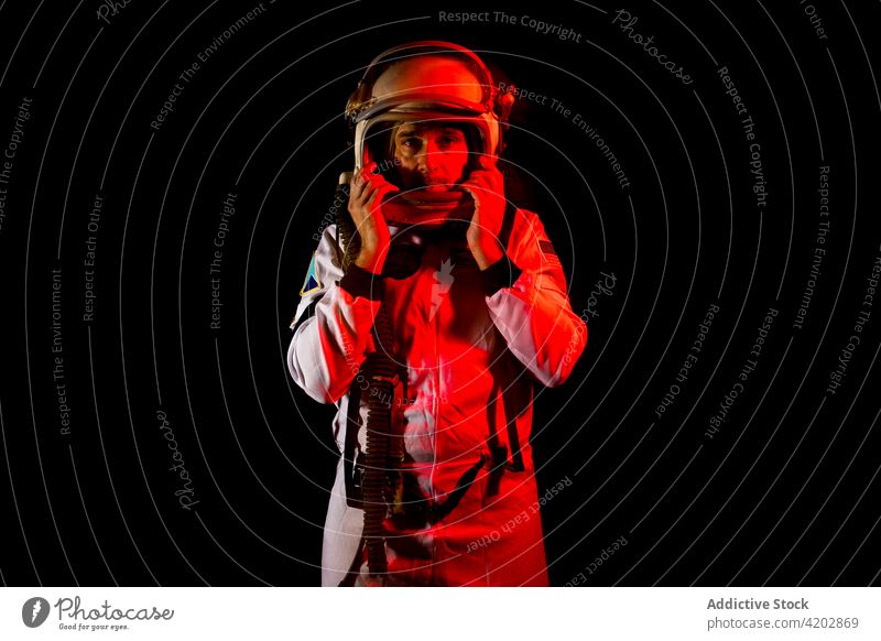 Astronaut in space suit standing in red neon light astronaut man helmet professional serious cosmonaut protective spacesuit armor spaceman mission safety dark