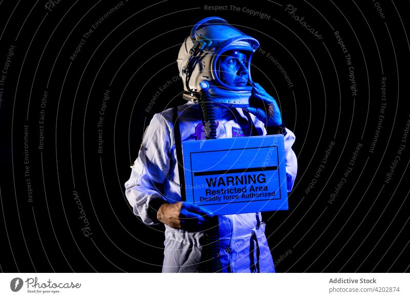 Serious astronaut in spacesuit showing placard with warning text demonstrate serious restricted area deadly force authorized cosmonaut caution attention safety