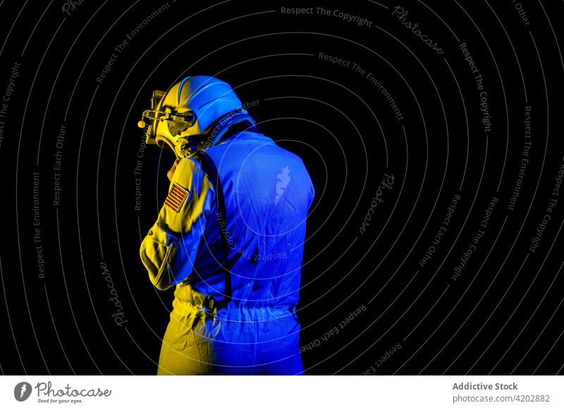 Astronaut in space suit standing in blue and yellow neon light astronaut man helmet professional cosmonaut protective spacesuit armor spaceman mission safety