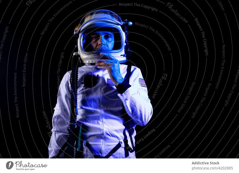 Astronaut in space suit standing in blue neon light astronaut man helmet professional serious cosmonaut protective spacesuit armor spaceman mission safety dark