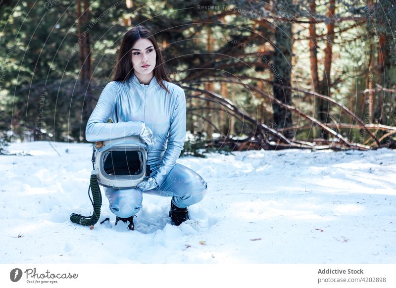 Attractive female astronaut crouched in snowy forest woman cosmonaut spacesuit calm winter astronomy helmet explorer unemotional professional serious protective