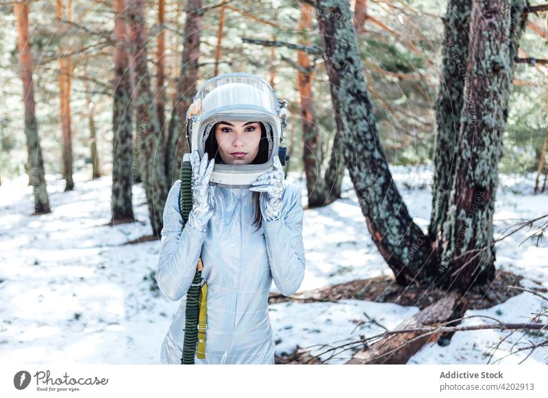 Determined female in space helmet standing in snowy forest astronaut spacesuit serious woman spacewoman cosmonaut winter astronomy beauty explorer unemotional