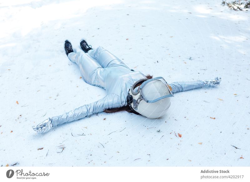 Woman in spacesuit lying on snowy glade in nature astronaut forest spacewoman cosmonaut armor costume calm winter astronomy helmet explorer unemotional