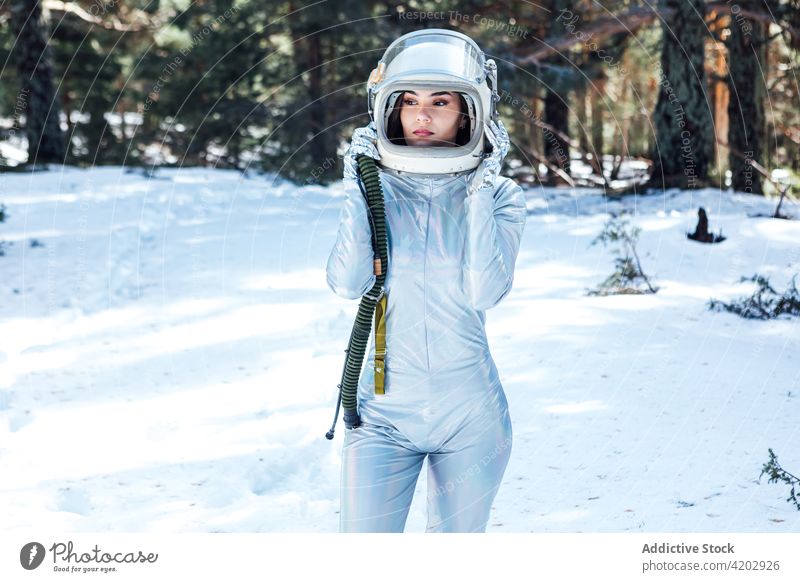 Determined female in space helmet standing in snowy forest astronaut spacesuit serious woman spacewoman cosmonaut winter astronomy beauty explorer unemotional