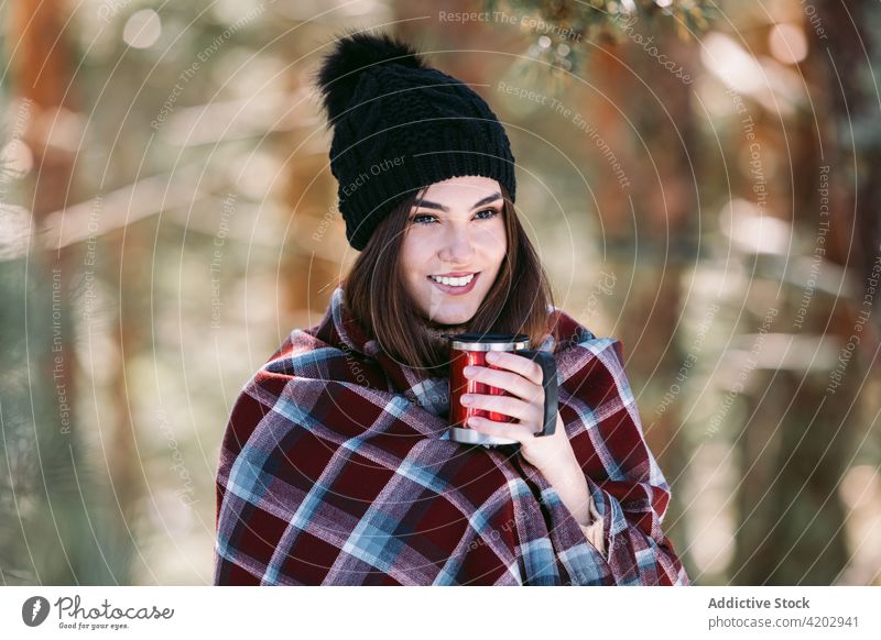 Woman sitting in winter woods and drinking coffee woman forest hot drink plaid wrap sunny trunk tree cup season enjoy frost mug beverage snow tea nature cold