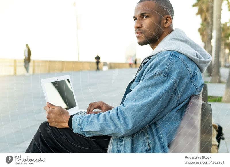 Black freelancer with laptop sitting in town employee masculine brutal macho contemplate man urban netbook work browsing convenient internet online natural
